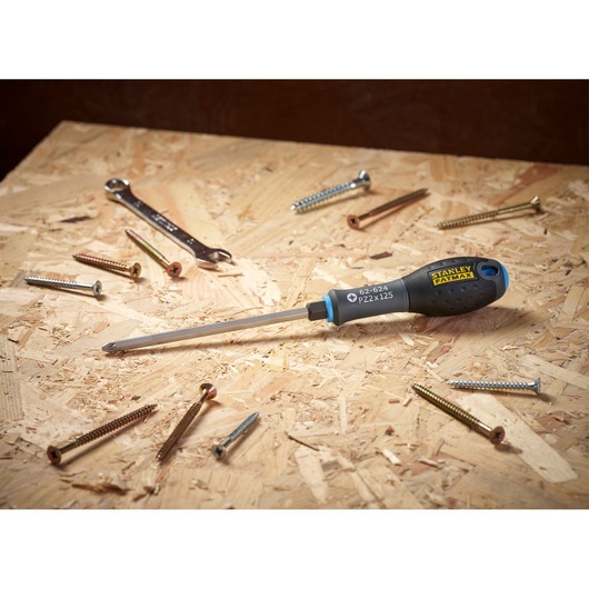 A STANLEY FATMAX screwdriver with a black and yellow handle is laying on a wooden surface, surrounded by several screws and a metal wrench.