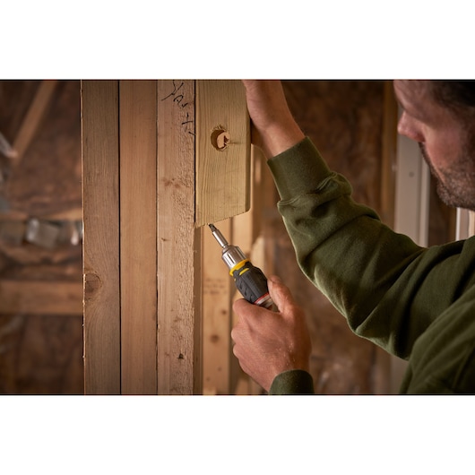 STANLEY FMHT0-62688 screwdriver used to fasten screw into wood frame, close-up view in construction setting.
