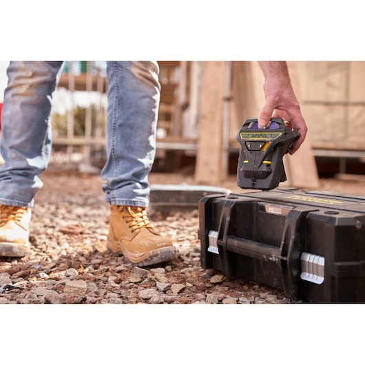 STANLEY FMHT1-77356 hand tool beside a black toolbox on rocky ground, outdoor construction setting.