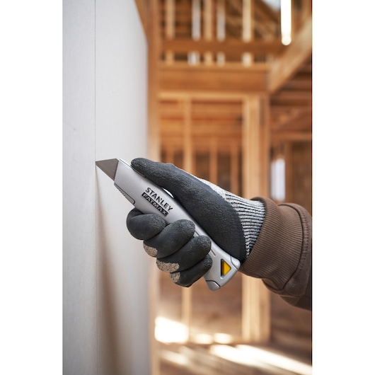 Photo of STANLEY FMHT10501-0 utility knife cutting drywall, shown in gloved hand at construction site.