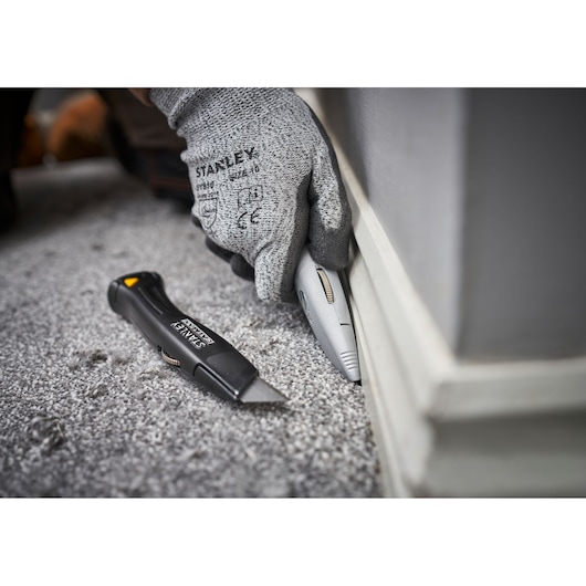 STANLEY FMHT10501-0 utility knife used to trim carpet near baseboard, close up photography.