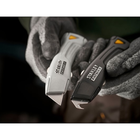 STANLEY FMHT10501-0 utility knives, FATMAX series, grey and black, held by gloved hands, product close-up.