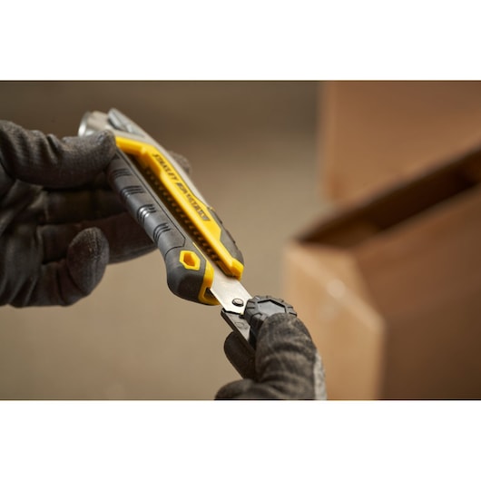 STANLEY FMHT10592-0 utility knife with yellow and black grip held by gloved hands near a cardboard box.