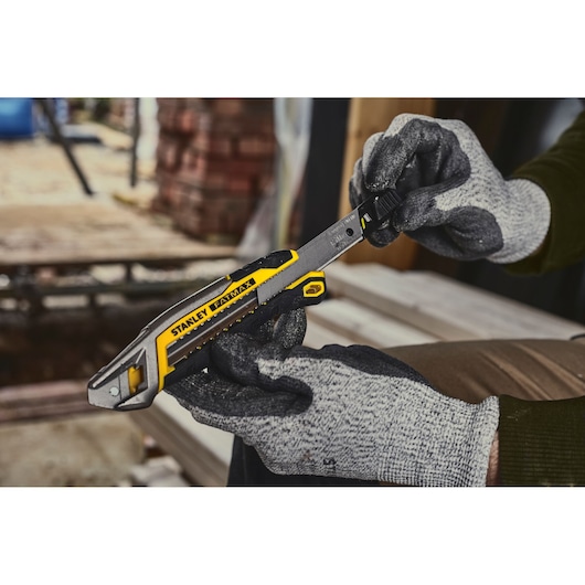 Photo of STANLEY FMHT10594-0 utility knife held by gloved hands at a construction site.
