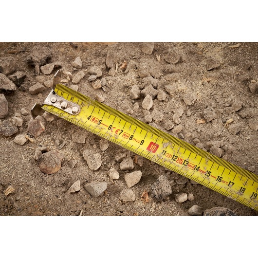 STANLEY FMHT38217-0 yellow tape measure photography showing close view on rocky soil.