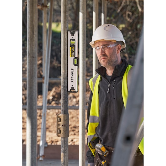 Photo of STANLEY FMHT43671-1 spirit level on metal scaffolding, construction worker in safety gear in background.
