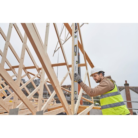 STANLEY FMHT43676-1 spirit level used by worker on wooden house frame at construction site.