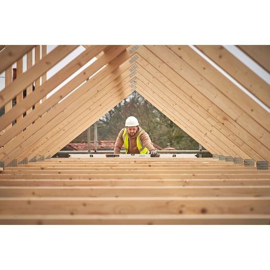 STANLEY FMHT43679-1 spirit level used by builder in wooden roof frame, wide angle, construction site.