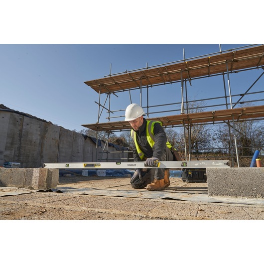 STANLEY FMHT43679-1 spirit level used by builder on construction site with blocks and scaffolding in background.