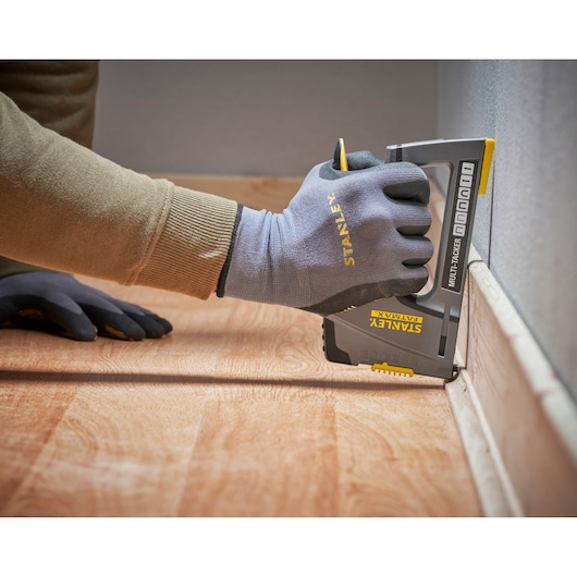 Photo of a hand wearing Stanley gloves using a STANLEY FMHT6-70868 multi-tacker on floor trim, side angle.