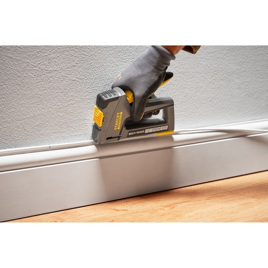 Photo of STANLEY FMHT6-70868 multi-tacker in use attaching trim to wall, held by gloved hand.