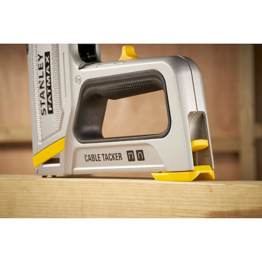 STANLEY FMHT70100-0 cable tacker, silver and yellow, side view on wooden beam.