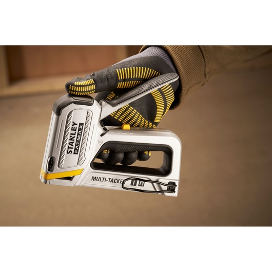 Photo of STANLEY FMHT70250-0 multi-tacker staple gun held in a gloved hand, close-up side view.