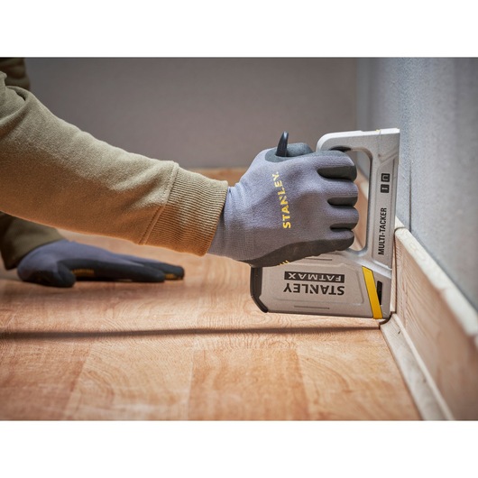 Photo of a gloved hand using a STANLEY FATMAX FMHT70443-0 multi-tacker stapler on flooring next to a wall.