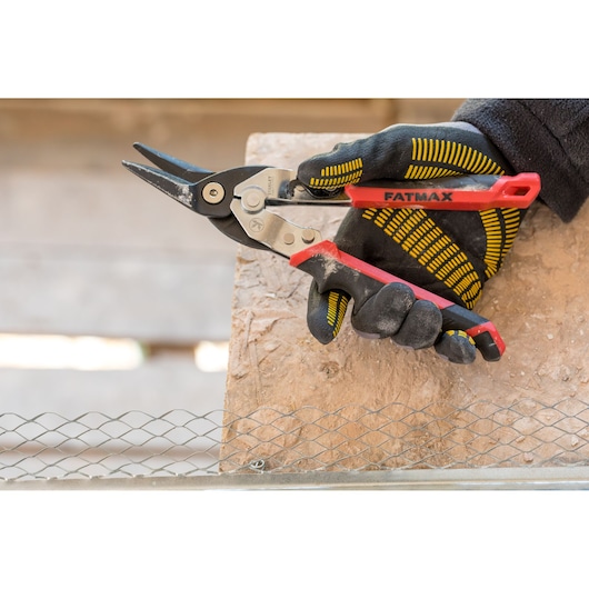 Stanley FMHT73755 metal snips with red handle in gloved hand, side angle, cutting wire mesh.