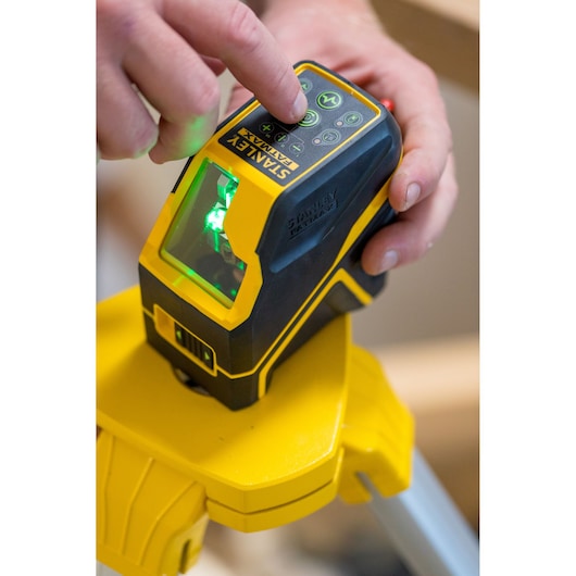 STANLEY FMHT77595-1 laser level on tripod, close-up of hand pressing control buttons with green laser on.