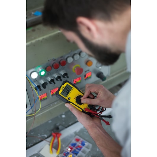Photo of STANLEY FMHT82565-0 digital multimeter being used to measure a control panel; yellow and black device.