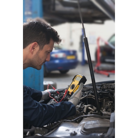 Photo of STANLEY FMHT82565-0 digital multimeter in use by mechanic testing car engine.