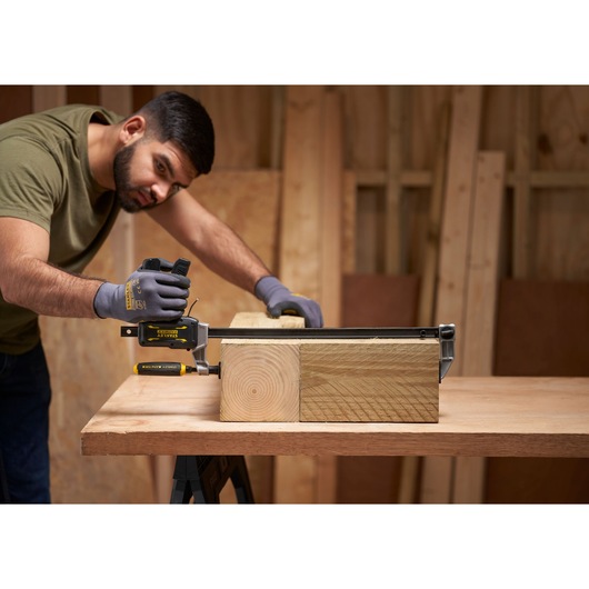 STANLEY FMHT83007-0 bar clamp being used to secure wooden beams on a workbench in a workshop setting.