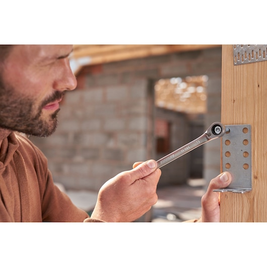 STANLEY FMMT82848-0 reversible ratcheting wrench in use tightening a bolt on a metal bracket attached to wood.