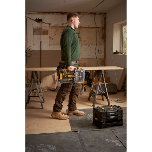Photo of STANLEY FMMT98101-0 tool organiser in clear and black plastic, shown being carried on a construction site.