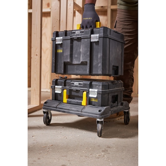 Stanley FMST1-71971 black tool box with yellow handle, side angle photo in workshop on wheeled platform.