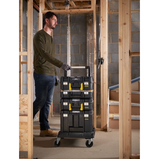 STANLEY FMST1-71972 rolling tool box stack with telescopic handle and yellow latches, shown in a construction site.
