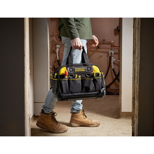 STANLEY FMST1-73607 tool bag with yellow accents, carried by person wearing work boots indoors.