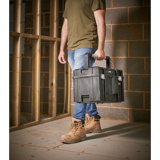STANLEY FMST1-75796 black toolbox carried by person on construction site, product category photography.