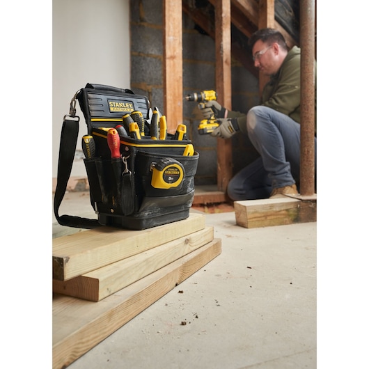 STANLEY FMST17624-1 tool bag filled with hand tools, tape measure, and drill, shown at a construction site.