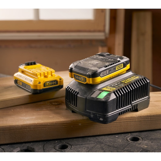 STANLEY SFMCB202 power tool battery and charger on wooden planks in workshop setting.
