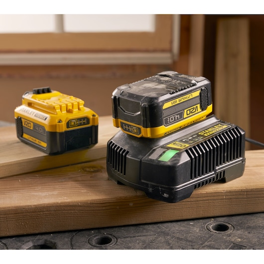 Photo of STANLEY SFMCB204 V20 4.0Ah lithium ion battery and charger, yellow and black, placed on wooden planks.