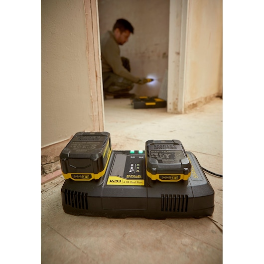 STANLEY SFMCB24 dual port charger with two V20 batteries on a floor in a construction setting.