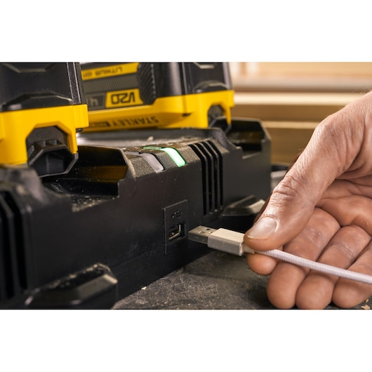 STANLEY SFMCB24 battery charger close-up with USB port, hand plugging in a USB cable, partial battery visible.