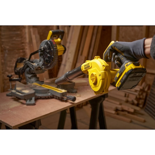 STANLEY SFMCBL01B cordless blower in use, yellow and black, cleaning wood dust in workshop.
