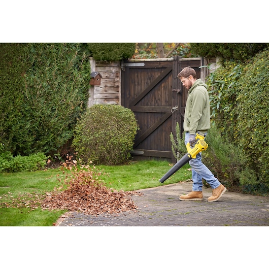 STANLEY SFMCBL714B-XJ leaf blower in use, blowing leaves on a garden path, side outdoor view.