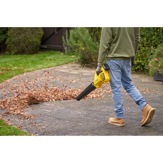 Photo of a person using a STANLEY SFMCBL714B-XJ cordless leaf blower on a patio covered with autumn leaves.