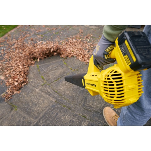 STANLEY SFMCBL714B-XJ cordless leaf blower in use, blowing leaves on stone pavement, close-up view.