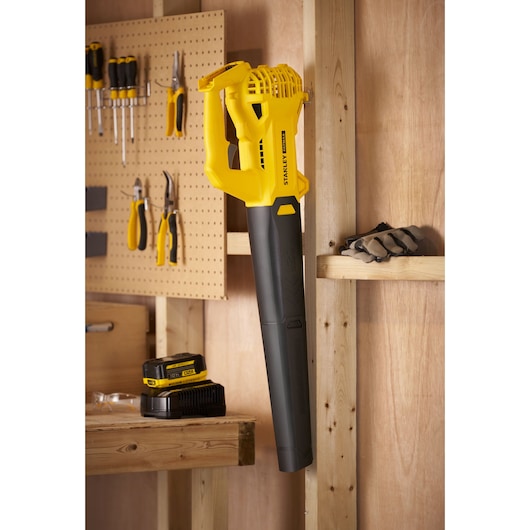 STANLEY SFMCBL714B-XJ cordless blower hanging in workshop, yellow and black color, side angle.