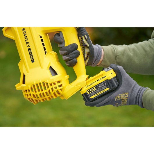 STANLEY SFMCBL714B-XJ cordless blower battery being inserted by gloved hands, close-up outdoor view.