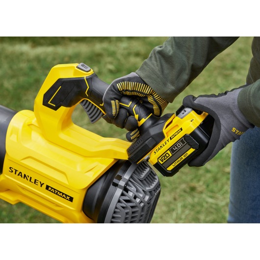 STANLEY SFMCBL730B leaf blower close-up, yellow handle and battery, outdoor use, person with gloves.