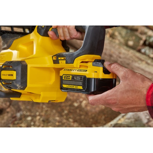 STANLEY SFMCCS630B chainsaw close up showing V20 lithium-ion 4.0Ah battery being attached outdoors.
