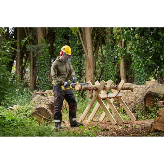 STANLEY SFMCCS730M1 cordless chainsaw in use outdoors cutting a log on a wooden sawhorse.