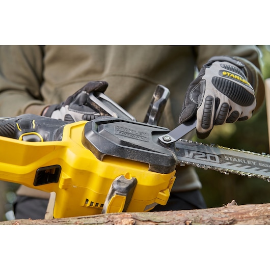 STANLEY SFMCCS730M1 chainsaw close-up, yellow body, V20 model, gloves adjusting chain outdoors.