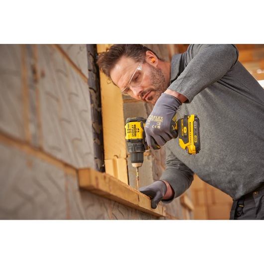 Photo of a person using a STANLEY SFMCD714B-XJ cordless drill, driving a screw into wood at a construction site.