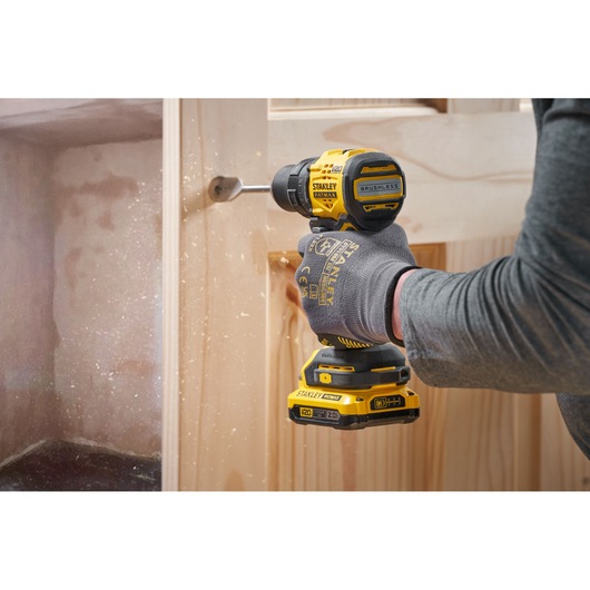 STANLEY SFMCD714B-XJ cordless drill in use, drilling into wood, side view, yellow and black power tool.