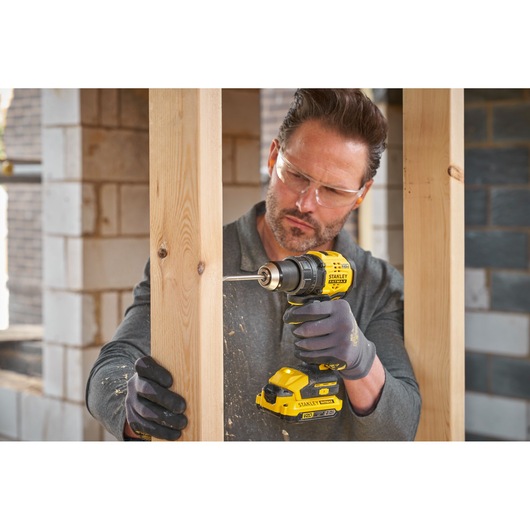 Photo of STANLEY SFMCD714B-XJ cordless drill in use drilling into wood at a construction site.