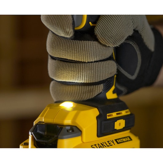 STANLEY SFMCD720B drill close-up, LED light on, gloved hand gripping handle, yellow and black.