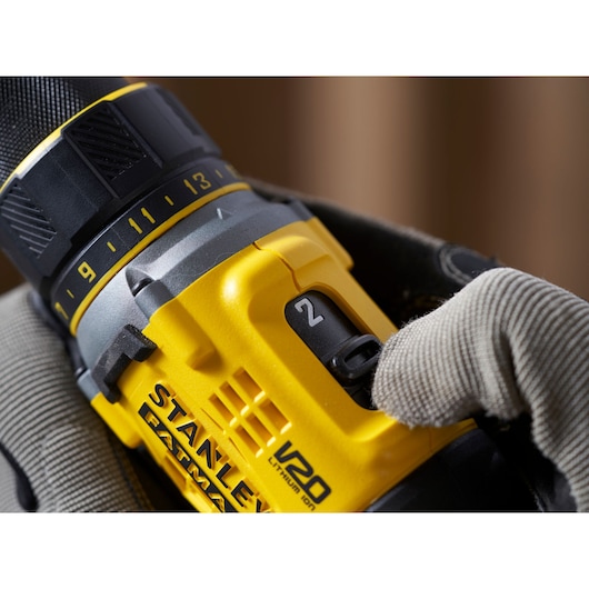 Close-up of STANLEY SFMCD720B cordless drill with V20 Lithium Ion label and gear switch, showing hand in glove.