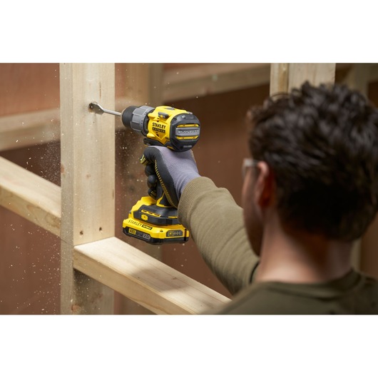 Photo of STANLEY SFMCD726B cordless drill in use, drilling through a wooden beam, side angle.